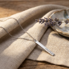 Zilveren rechthoekige staafvormige hanger met naam gravure aan zilveren ketting liggend op linnen doek met lavendel lifestyle modelfoto gepersonaliseerd zilveren naamketting sieraad