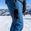 Telefoon aan een uitrolbaar koord aan een blauwe skibroek, met de piste en een stoeltjeslift op de achtergrond