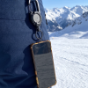 Telefoon aan een koord met karabijnhaak aan een skibroek, bergen en sneeuw op de achtergrond